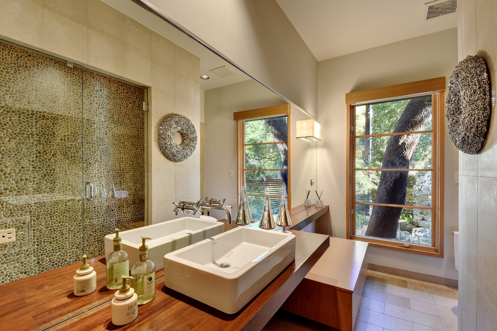 Foto de cuarto de baño actual con ducha empotrada, suelo de baldosas tipo guijarro, paredes beige, aseo y ducha, lavabo sobreencimera y encimera de madera