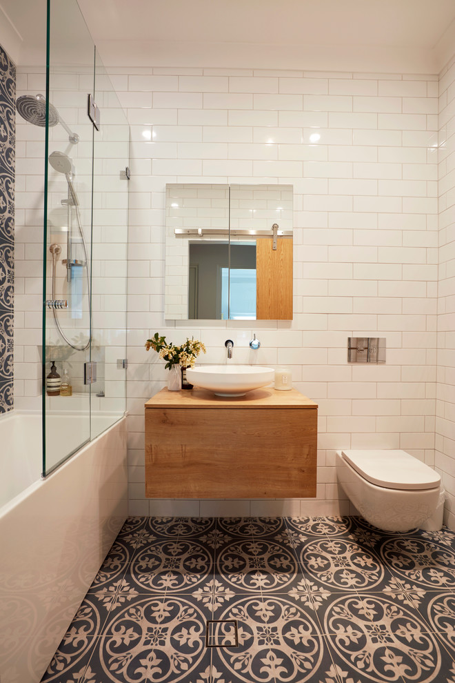 Imagen de cuarto de baño principal, actual, pequeño, con puertas de armario de madera oscura, combinación de ducha y bañera, sanitario de pared, baldosas y/o azulejos azules, baldosas y/o azulejos blancos, paredes blancas, suelo de baldosas de cerámica, lavabo sobreencimera, encimera de madera, armarios con paneles lisos, bañera empotrada, ducha abierta y encimeras marrones