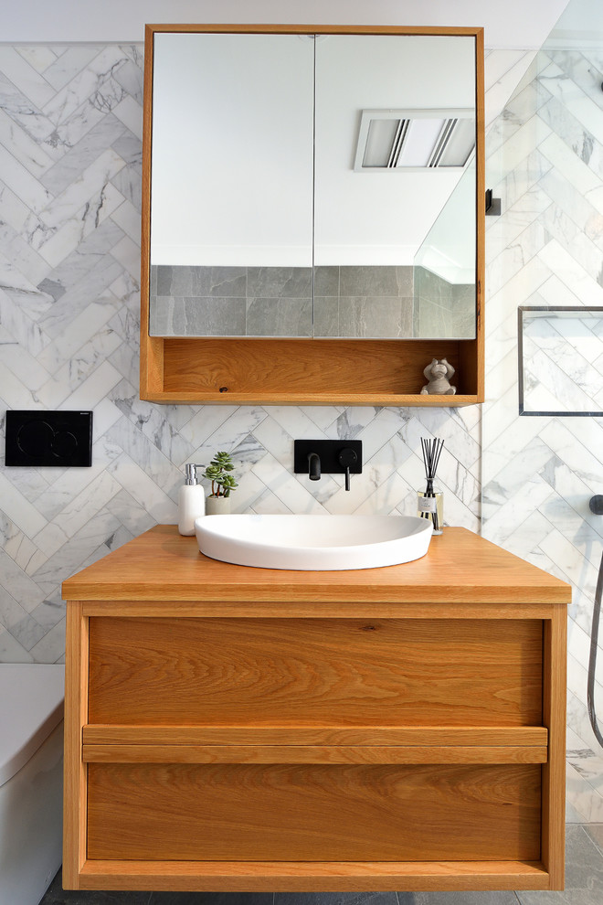 На фото: маленькая главная ванная комната в стиле модернизм с фасадами островного типа, светлыми деревянными фасадами, душевой комнатой, унитазом-моноблоком, белой плиткой, цементной плиткой, серыми стенами, полом из керамической плитки, настольной раковиной, столешницей из дерева, серым полом, душем с распашными дверями и коричневой столешницей для на участке и в саду