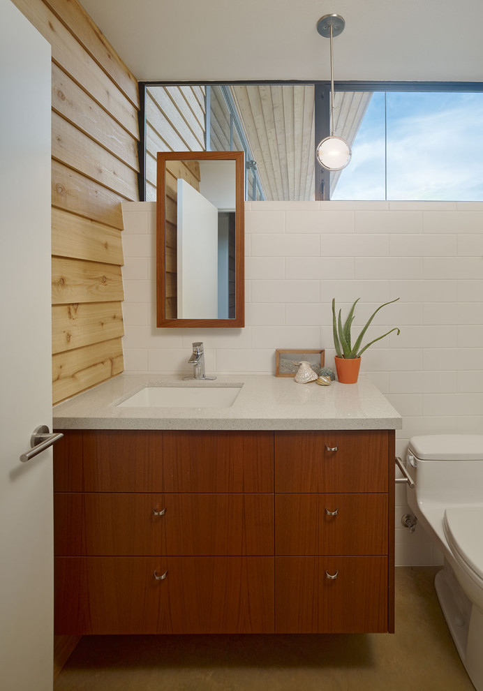 Foto på ett funkis badrum, med ett undermonterad handfat, släta luckor, skåp i mellenmörkt trä, en toalettstol med hel cisternkåpa, vit kakel och tunnelbanekakel
