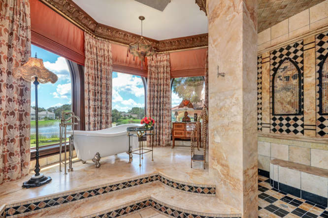 Идея дизайна: огромная главная ванная комната в средиземноморском стиле с фасадами с выступающей филенкой, искусственно-состаренными фасадами, ванной на ножках, унитазом-моноблоком, бежевой плиткой, каменной плиткой, бежевыми стенами, полом из травертина, врезной раковиной, столешницей из оникса, желтым полом и душем с распашными дверями