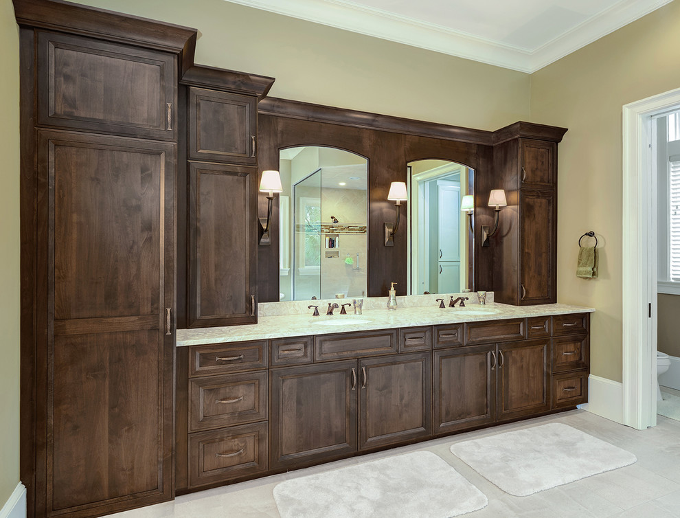 Cette image montre une grande salle de bain traditionnelle en bois brun avec un lavabo encastré, un placard avec porte à panneau encastré, un plan de toilette en marbre et un sol en carrelage de céramique.