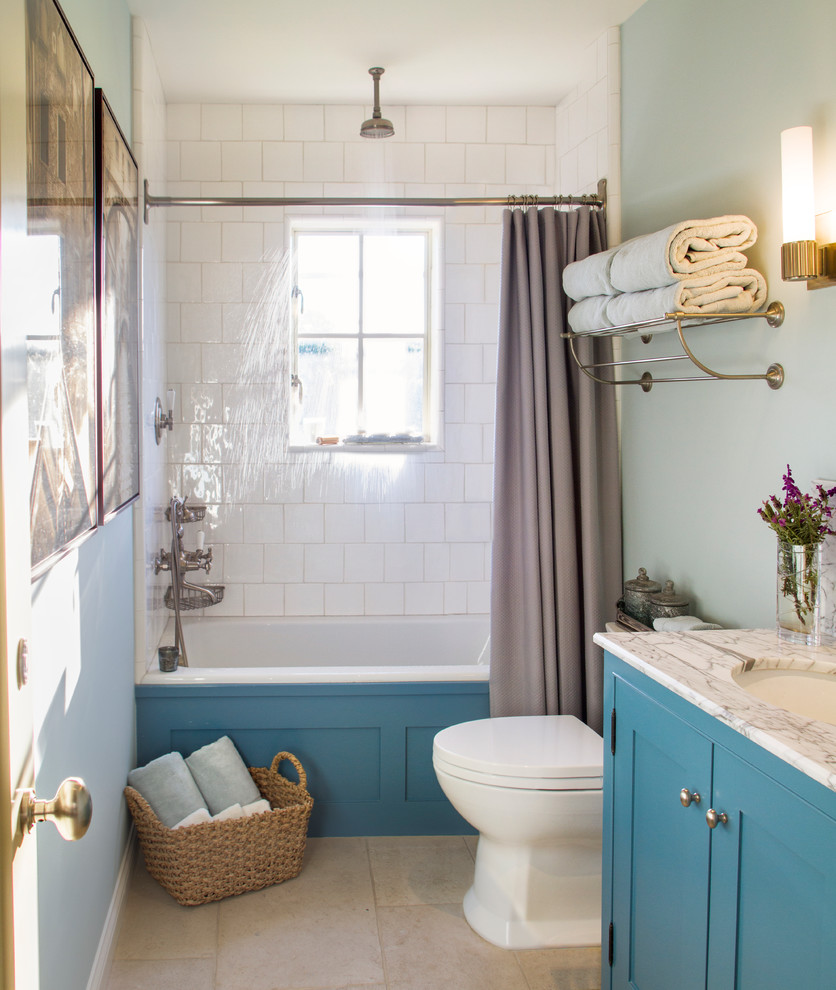 Aménagement d'une salle de bain campagne avec un placard à porte shaker, des portes de placard bleues, une baignoire en alcôve, un combiné douche/baignoire, WC séparés, un carrelage blanc, un carrelage métro, un lavabo encastré, un plan de toilette en marbre, un mur bleu, une cabine de douche avec un rideau, un plan de toilette blanc, un sol en calcaire et un sol beige.