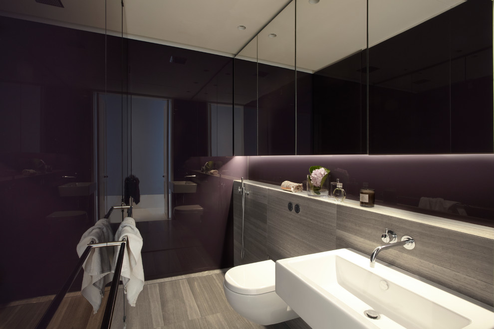 Bild på ett funkis badrum, med en vägghängd toalettstol, ett väggmonterat handfat, en dusch i en alkov, grå kakel och beiget golv