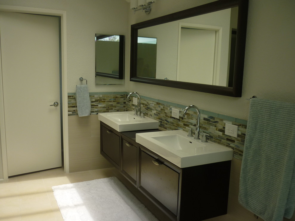 This is an example of a medium sized contemporary ensuite bathroom in Orange County with an integrated sink, dark wood cabinets, glass worktops, beige tiles, porcelain tiles, grey walls, porcelain flooring, flat-panel cabinets, a freestanding bath, a corner shower, beige floors and a hinged door.
