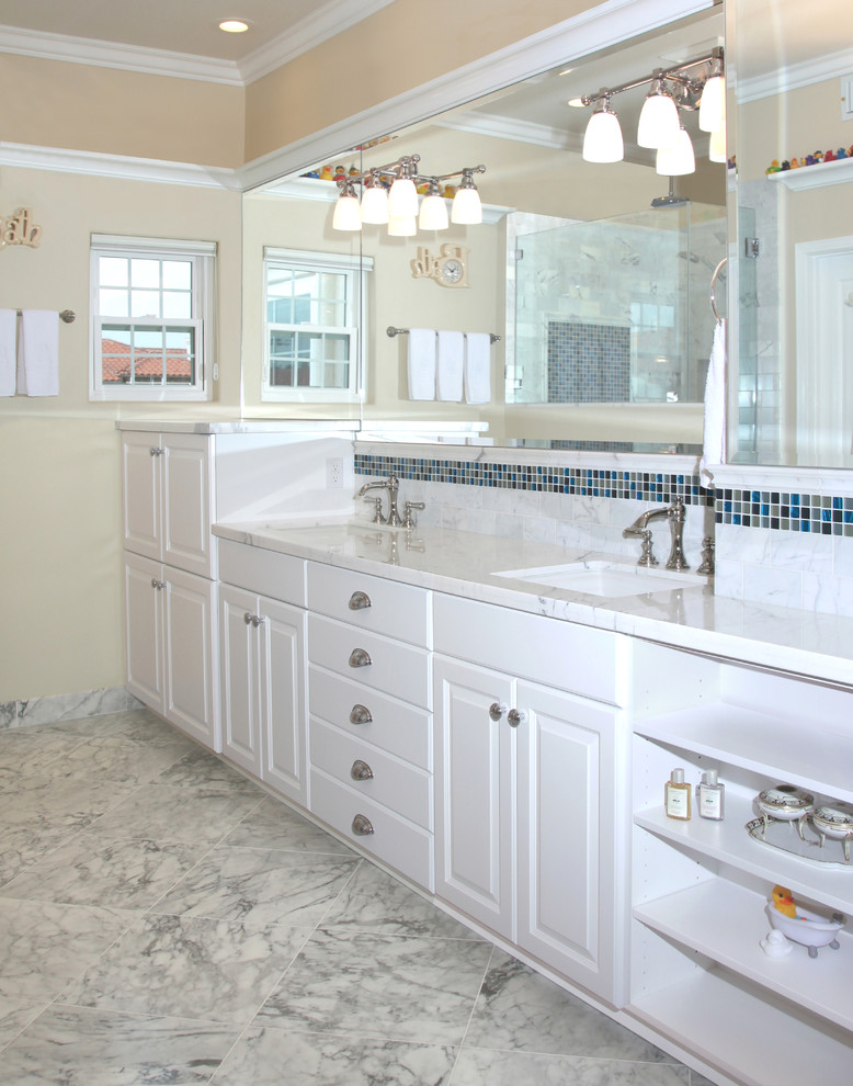 Ispirazione per una stanza da bagno padronale classica con ante con bugna sagomata, ante bianche, pareti beige, pavimento in marmo, lavabo sottopiano e top in marmo