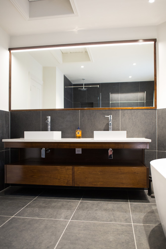 Medium sized contemporary family bathroom in London with dark wood cabinets, a freestanding bath, a walk-in shower, a wall mounted toilet, grey tiles, stone tiles, white walls, porcelain flooring, a wall-mounted sink, marble worktops, grey floors, an open shower and white worktops.