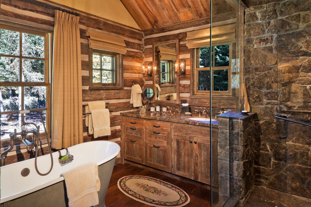 Cette image montre une salle de bain chalet avec une baignoire indépendante, un plan de toilette en granite et un mur en pierre.