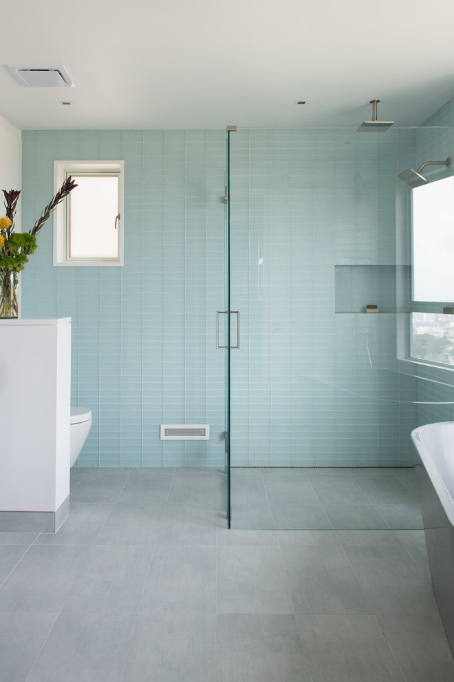 Bild på ett litet funkis badrum, med ett integrerad handfat, släta luckor, skåp i mellenmörkt trä, ett fristående badkar, en kantlös dusch, en vägghängd toalettstol, grå kakel, glaskakel, vita väggar och klinkergolv i porslin
