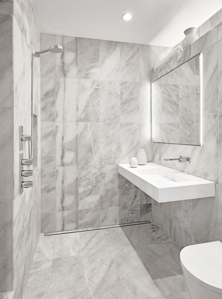 Modern inredning av ett litet badrum, med öppna hyllor, en vägghängd toalettstol, grå kakel, marmorkakel, grå väggar, marmorgolv, ett väggmonterat handfat, bänkskiva i akrylsten, grått golv och med dusch som är öppen