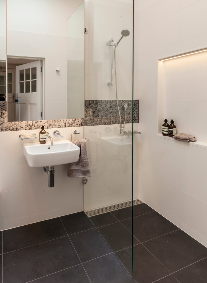 Bild på ett litet funkis badrum med dusch, med luckor med glaspanel, en dusch i en alkov, en vägghängd toalettstol, vit kakel, cementkakel, vita väggar, klinkergolv i keramik, ett väggmonterat handfat, grått golv och med dusch som är öppen