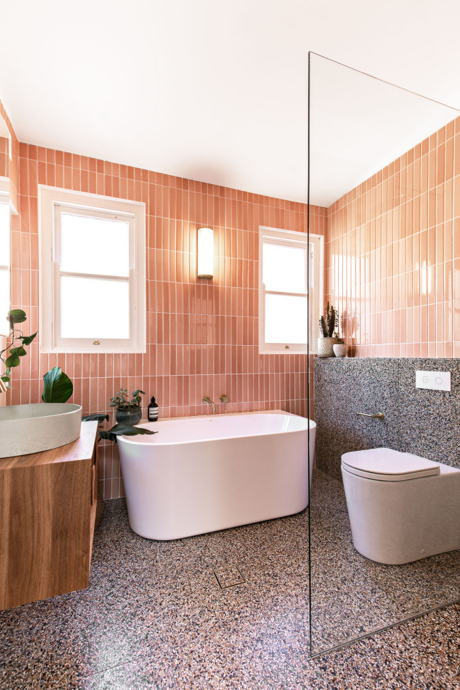 На фото: главная ванная комната среднего размера в скандинавском стиле с фасадами цвета дерева среднего тона, отдельно стоящей ванной, открытым душем, раздельным унитазом, розовой плиткой, керамической плиткой, розовыми стенами, полом из терраццо, подвесной раковиной, столешницей из дерева, разноцветным полом, открытым душем, коричневой столешницей, тумбой под одну раковину и подвесной тумбой