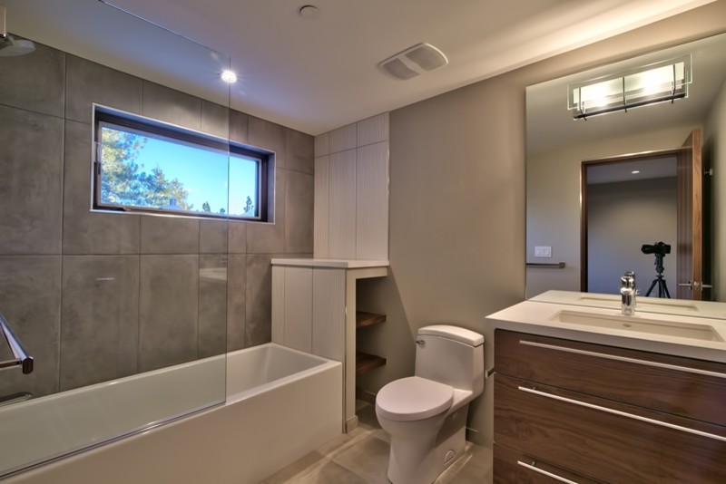 Idéer för ett mellanstort modernt badrum med dusch, med släta luckor, skåp i mellenmörkt trä, grå kakel, grå väggar, vinylgolv, ett badkar i en alkov, en dusch/badkar-kombination, en toalettstol med hel cisternkåpa, keramikplattor, ett undermonterad handfat och bänkskiva i akrylsten