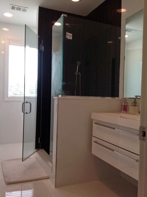 На фото: ванная комната среднего размера в современном стиле с плоскими фасадами, белыми фасадами, угловым душем, черной плиткой, керамической плиткой, белыми стенами, монолитной раковиной и столешницей из искусственного камня