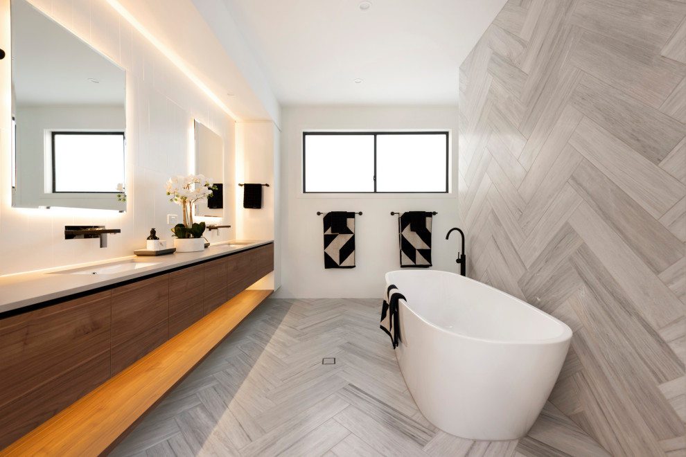 Идея дизайна: ванная комната в современном стиле с плоскими фасадами, темными деревянными фасадами, отдельно стоящей ванной, серой плиткой, белыми стенами, врезной раковиной, серым полом и серой столешницей