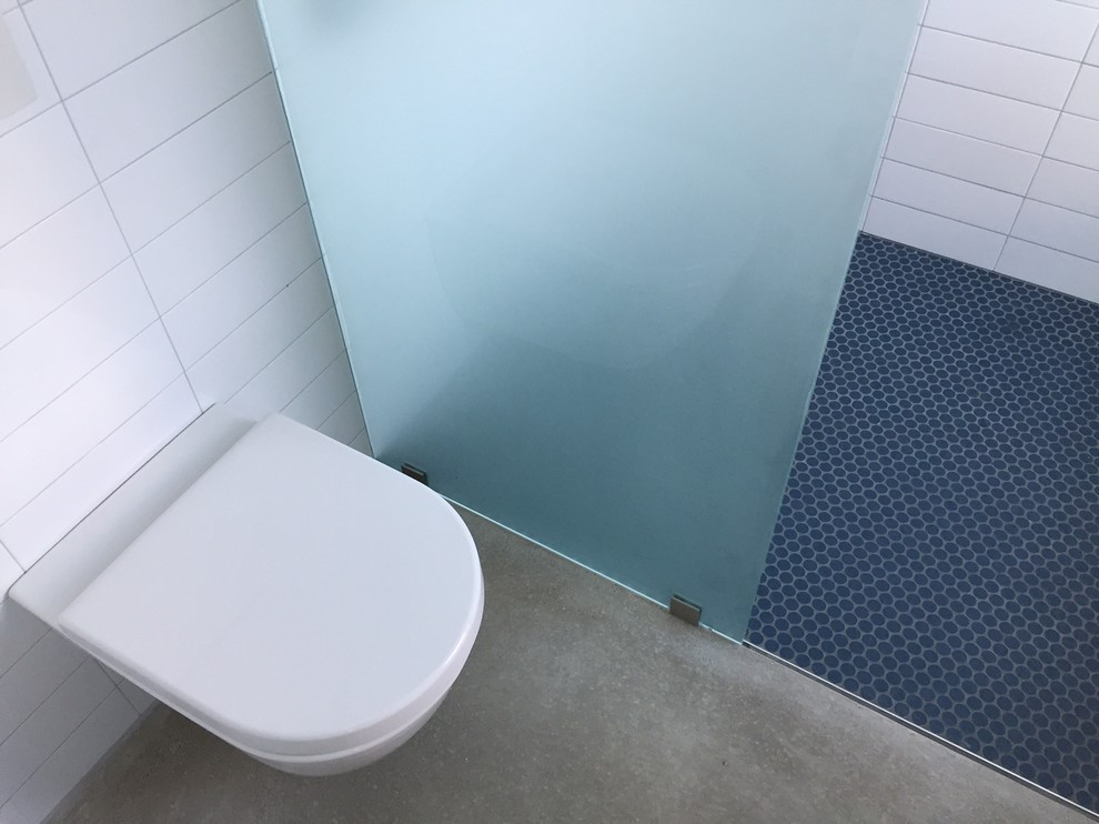 Foto på ett litet industriellt badrum, med en hörndusch, en vägghängd toalettstol, blå kakel, keramikplattor och vita väggar