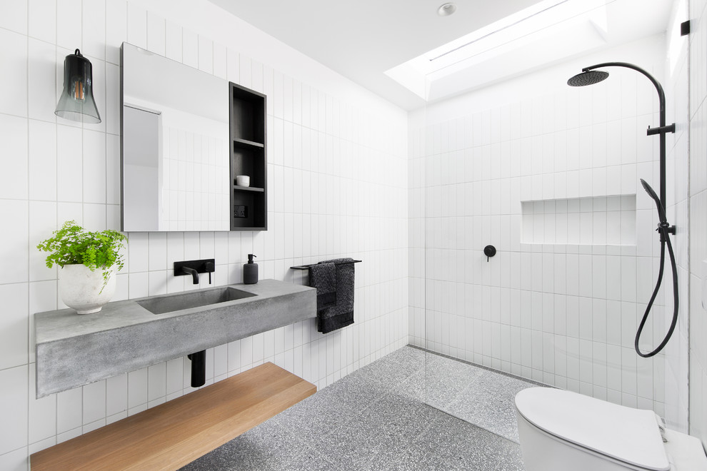 Modelo de cuarto de baño moderno con ducha a ras de suelo, baldosas y/o azulejos blancos, lavabo integrado, encimera de cemento, suelo gris, ducha abierta y encimeras grises