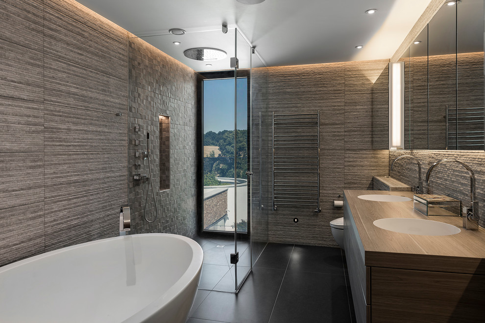 This is an example of a medium sized contemporary ensuite bathroom in Hampshire with flat-panel cabinets, medium wood cabinets, a freestanding bath, a walk-in shower, a wall mounted toilet, brown tiles, stone tiles, brown walls, porcelain flooring, a console sink and wooden worktops.