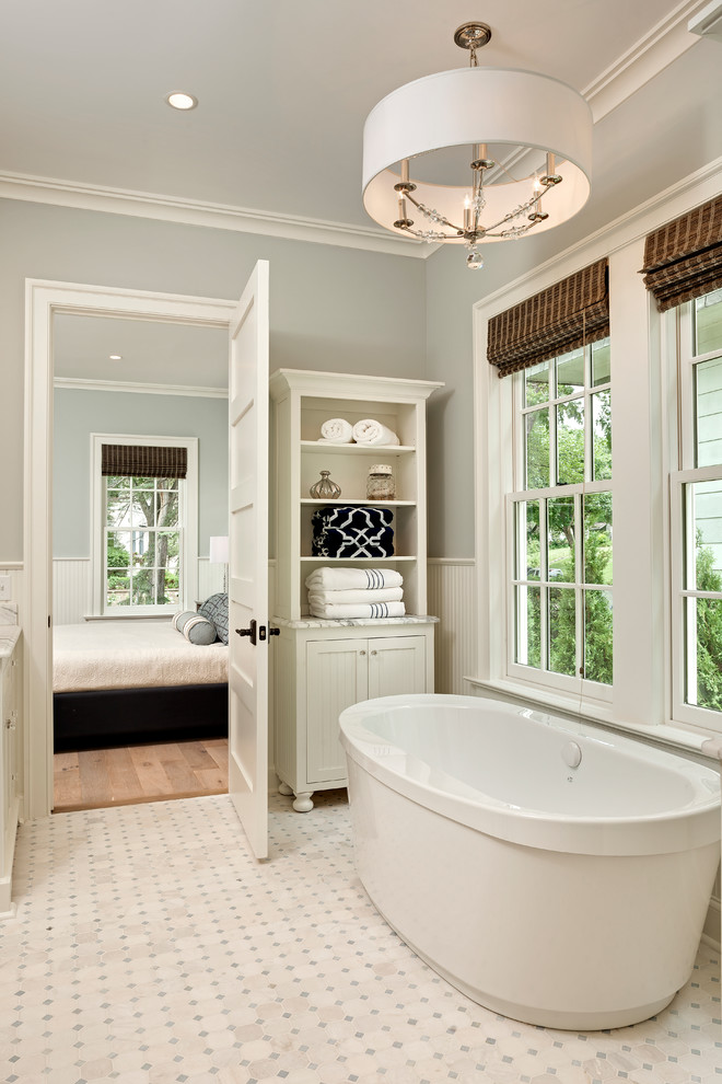 Bild på ett stort maritimt en-suite badrum, med luckor med profilerade fronter, vita skåp, marmorbänkskiva, ett fristående badkar, vit kakel, glaskakel, grå väggar och marmorgolv