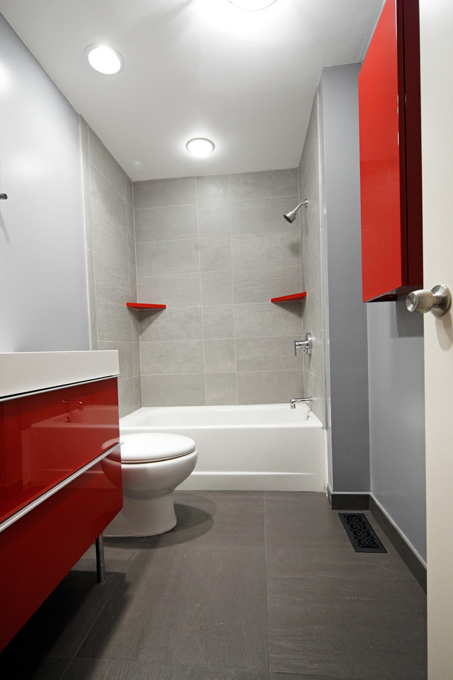 Inspiration för mellanstora moderna badrum för barn, med släta luckor, röda skåp, ett badkar i en alkov, en dusch/badkar-kombination, en toalettstol med separat cisternkåpa, grå kakel, porslinskakel, blå väggar, klinkergolv i porslin, ett integrerad handfat och bänkskiva i akrylsten