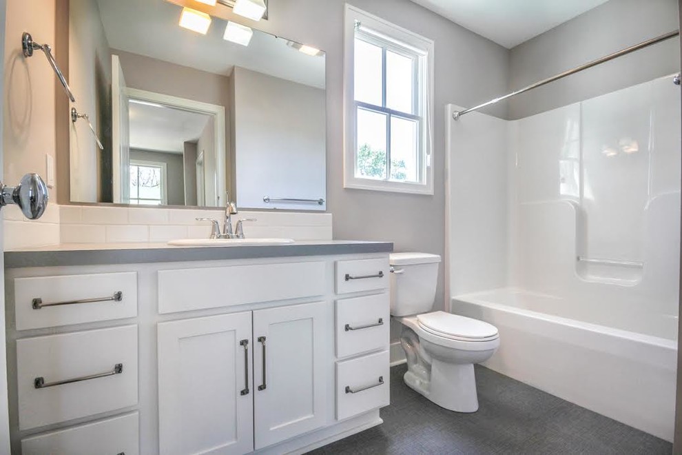 Klassisk inredning av ett mellanstort badrum med dusch, med skåp i shakerstil, vita skåp, ett badkar i en alkov, en dusch/badkar-kombination, en toalettstol med hel cisternkåpa, vit kakel, tunnelbanekakel, grå väggar, vinylgolv, ett nedsänkt handfat, bänkskiva i kvartsit, grått golv och dusch med duschdraperi