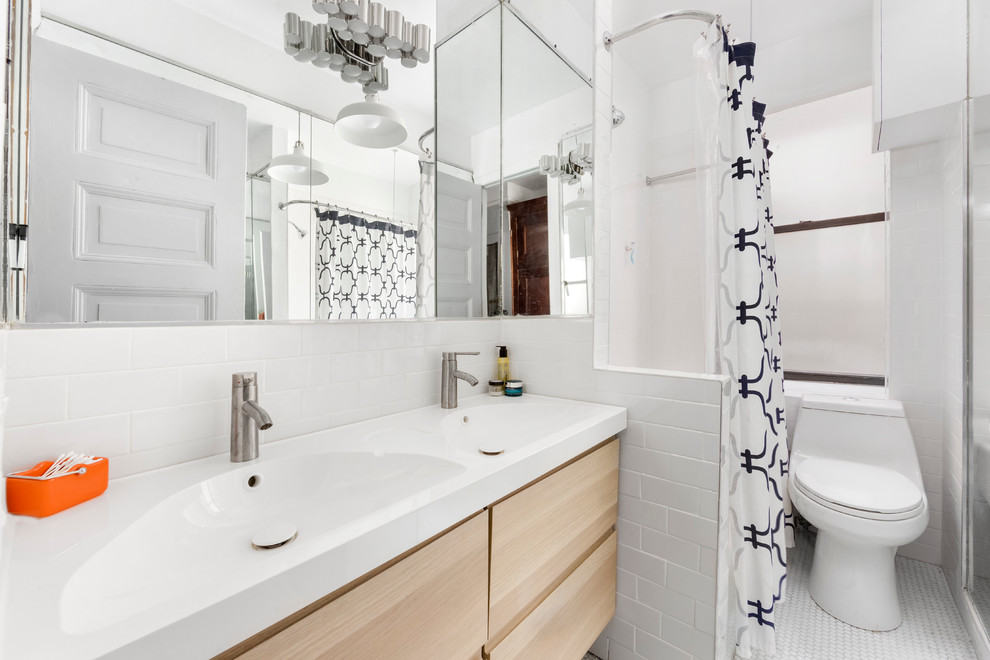 Cette photo montre une petite salle de bain principale tendance en bois clair avec un placard à porte plane, un combiné douche/baignoire, WC à poser, un carrelage blanc, un carrelage métro, un mur blanc, un plan vasque et un plan de toilette en surface solide.