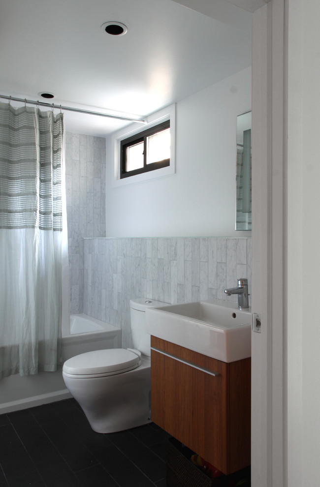 Diseño de cuarto de baño moderno con lavabo suspendido, armarios con paneles lisos, puertas de armario de madera oscura, bañera empotrada, combinación de ducha y bañera, sanitario de dos piezas y baldosas y/o azulejos blancos