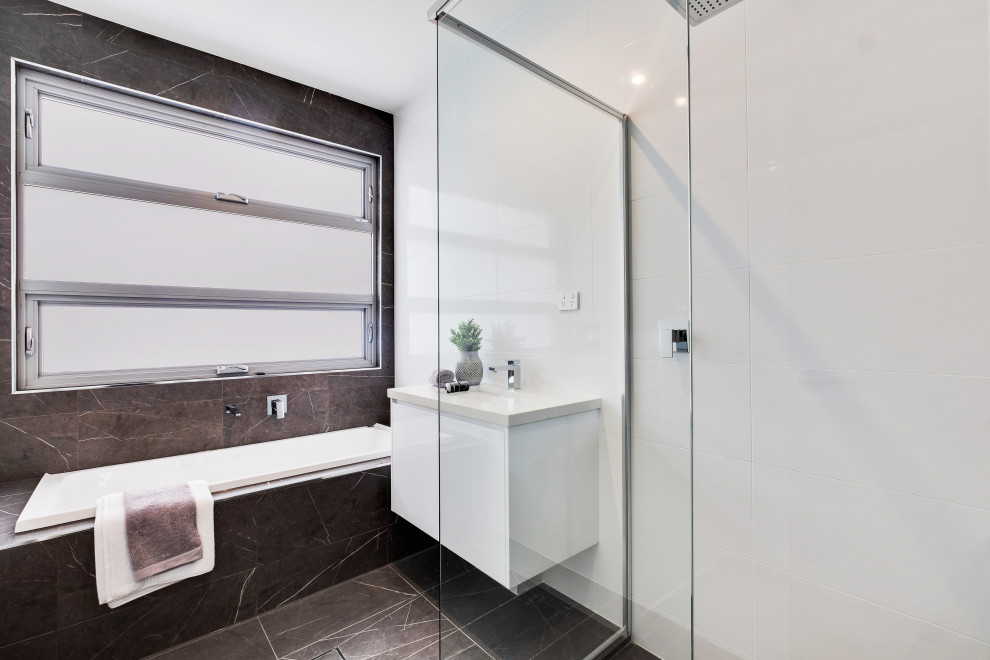 Aménagement d'une salle de bain contemporaine de taille moyenne avec un sol gris, un placard à porte plane, des portes de placard blanches, une baignoire posée, un carrelage blanc, un lavabo encastré et un plan de toilette blanc.