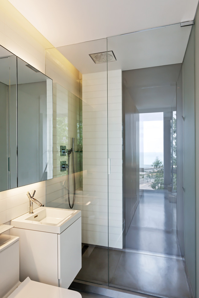 Idéer för små funkis en-suite badrum, med släta luckor, vita skåp, en öppen dusch, en toalettstol med separat cisternkåpa, vit kakel, glaskakel, vita väggar, betonggolv, ett integrerad handfat och bänkskiva i akrylsten