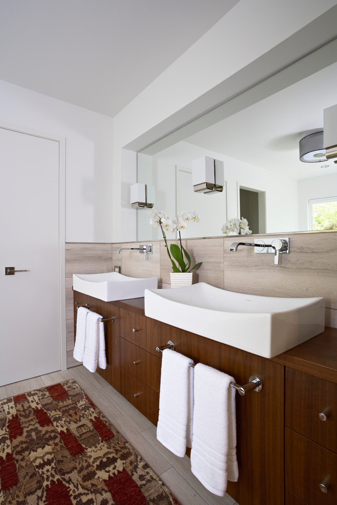 На фото: главная ванная комната в стиле модернизм с настольной раковиной, плоскими фасадами, темными деревянными фасадами, столешницей из дерева, бежевой плиткой, плиткой из листового камня и белыми стенами