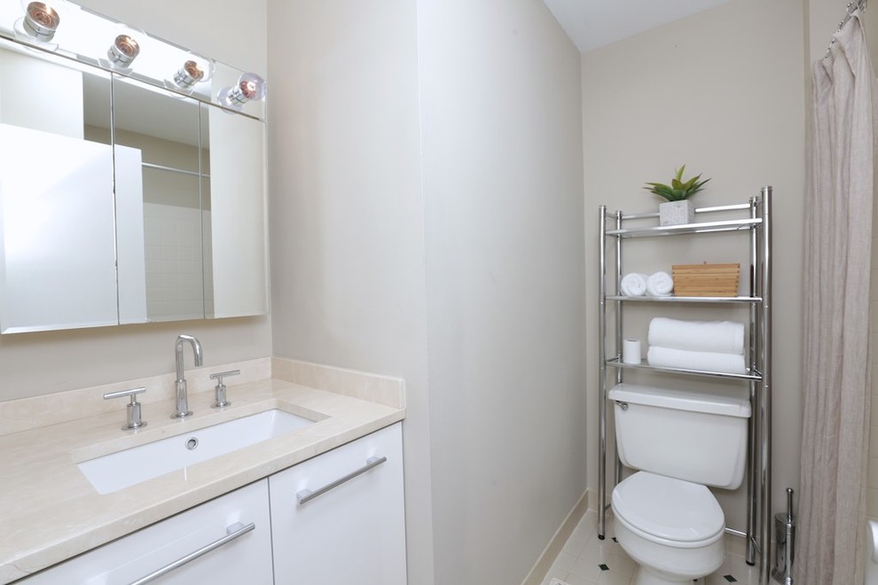 This is an example of a small modern bathroom in Philadelphia with flat-panel cabinets, white cabinets, an alcove bath, a shower/bath combination, a two-piece toilet, beige walls, ceramic flooring, a submerged sink, granite worktops, white floors and a shower curtain.