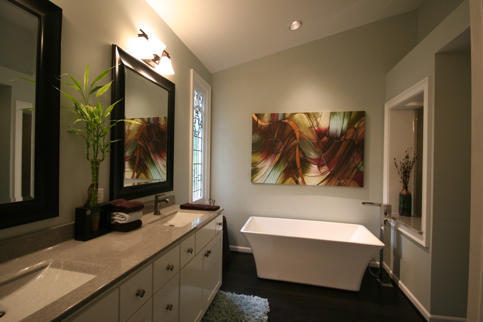 Modelo de cuarto de baño principal clásico renovado grande con armarios estilo shaker, puertas de armario blancas, bañera exenta, paredes grises, suelo de madera oscura, lavabo integrado y encimera de cuarzo compacto
