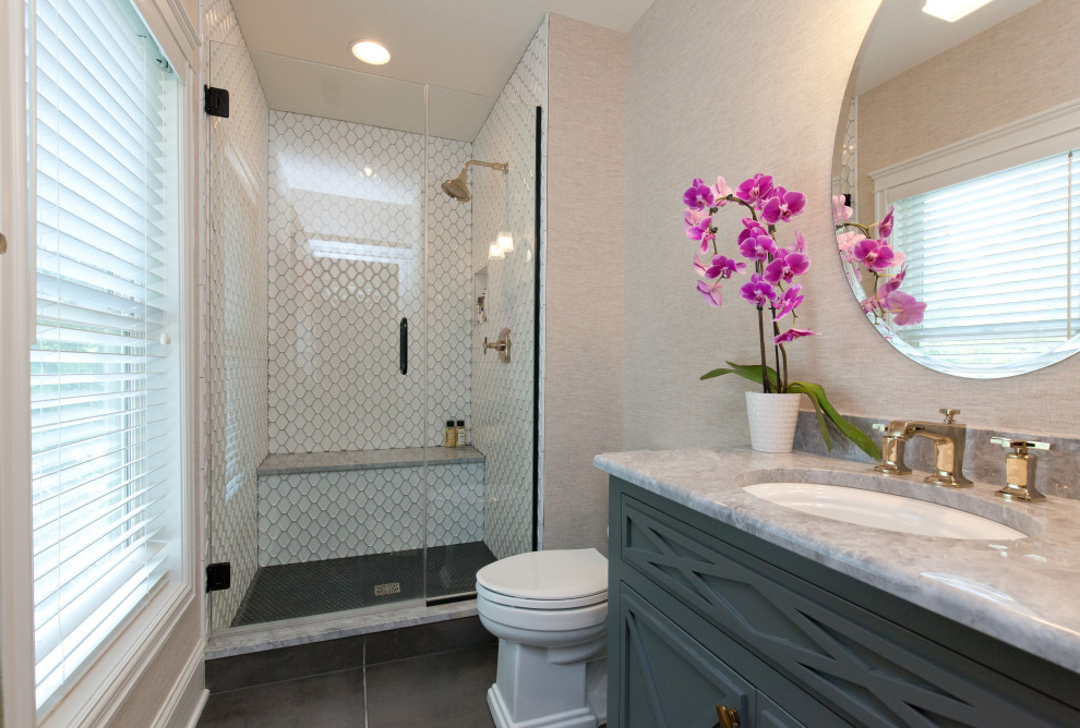 Inredning av ett klassiskt grå grått badrum, med möbel-liknande, grå skåp, en dusch i en alkov, en toalettstol med separat cisternkåpa, vit kakel, porslinskakel, vita väggar, klinkergolv i porslin, ett undermonterad handfat, bänkskiva i kvarts, grått golv och dusch med gångjärnsdörr