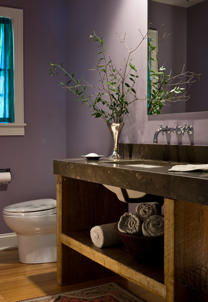 Cette photo montre une petite salle de bain chic avec un lavabo encastré, un plan de toilette en calcaire, WC à poser, un mur violet et un sol en bois brun.