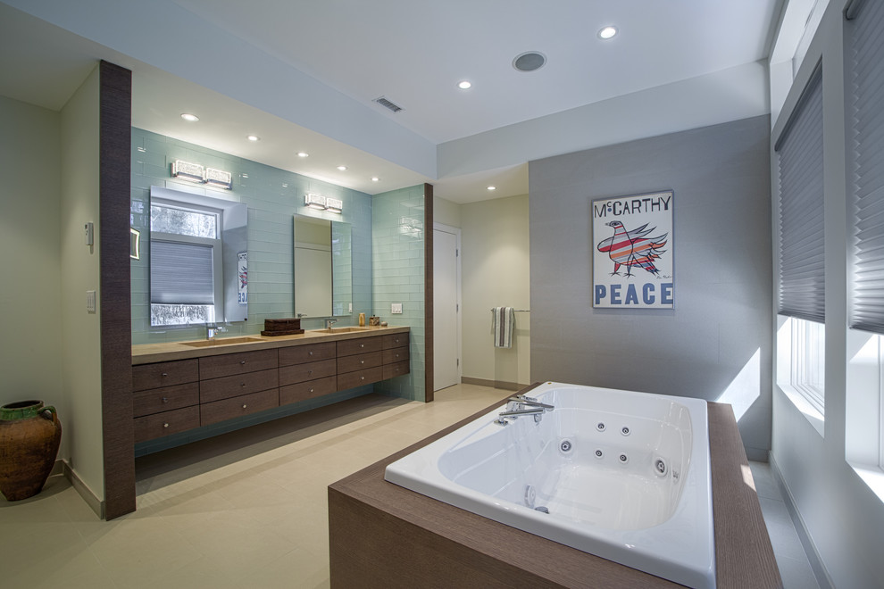 Пример оригинального дизайна: главная ванная комната среднего размера в стиле модернизм с плоскими фасадами, темными деревянными фасадами, гидромассажной ванной, зеленой плиткой, стеклянной плиткой, серыми стенами, светлым паркетным полом, монолитной раковиной и столешницей из искусственного камня