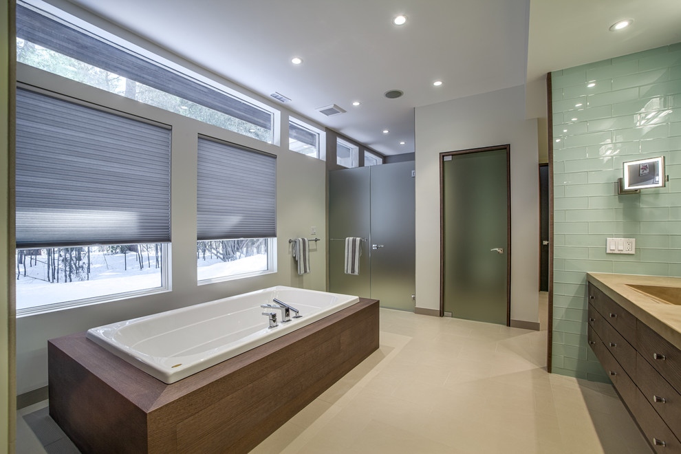 Bild på ett mellanstort funkis en-suite badrum, med släta luckor, skåp i mörkt trä, en jacuzzi, en dubbeldusch, grön kakel, glaskakel, grå väggar, ljust trägolv, ett integrerad handfat och bänkskiva i akrylsten