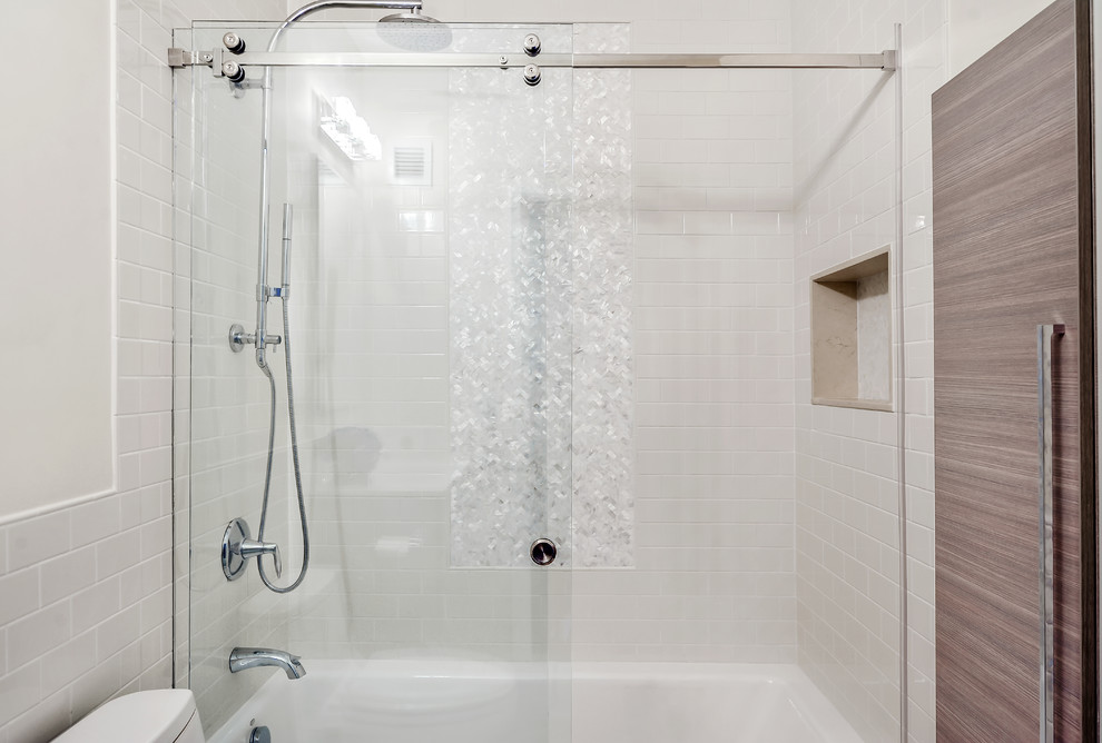 ニューヨークにある低価格の中くらいなトランジショナルスタイルのおしゃれなバスルーム (浴槽なし) (フラットパネル扉のキャビネット、中間色木目調キャビネット、アルコーブ型浴槽、シャワー付き浴槽	、一体型トイレ	、セラミックタイルの床、人工大理石カウンター、白いタイル、サブウェイタイル、白い壁、一体型シンク) の写真