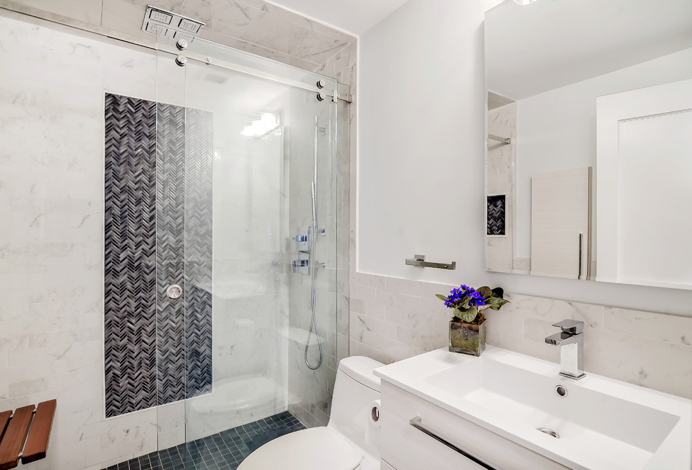 Example of a mid-sized transitional master gray tile and ceramic tile ceramic tile alcove shower design in New York with flat-panel cabinets, white cabinets, a one-piece toilet, a console sink, solid surface countertops and white walls
