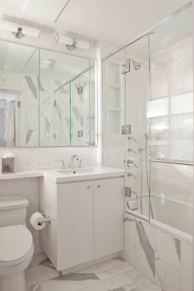 Klassisk inredning av ett badrum, med ett undermonterad handfat, släta luckor, vita skåp, ett badkar i en alkov, en dusch/badkar-kombination och vit kakel