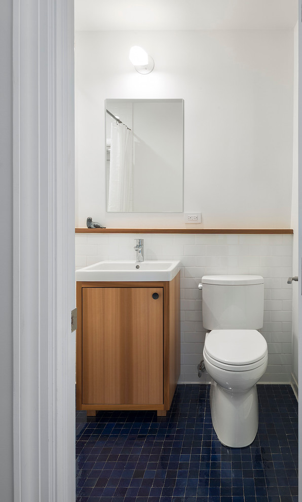 Modern inredning av ett badrum, med ett konsol handfat, släta luckor, skåp i mellenmörkt trä, vit kakel, tunnelbanekakel, vita väggar och blått golv
