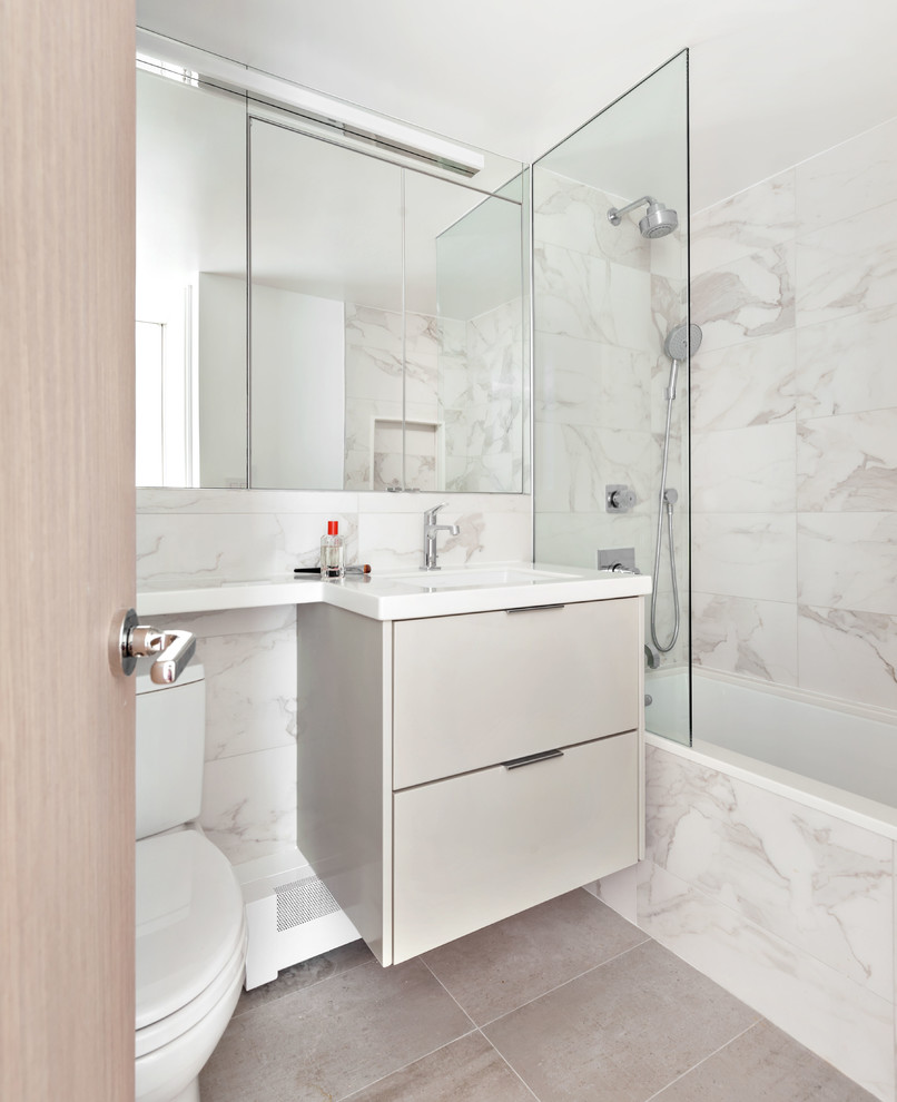 Bild på ett litet funkis vit vitt badrum, med släta luckor, grå skåp, ett badkar i en alkov, en dusch/badkar-kombination, grå kakel, porslinskakel, marmorgolv, ett undermonterad handfat, bänkskiva i akrylsten, grått golv och med dusch som är öppen