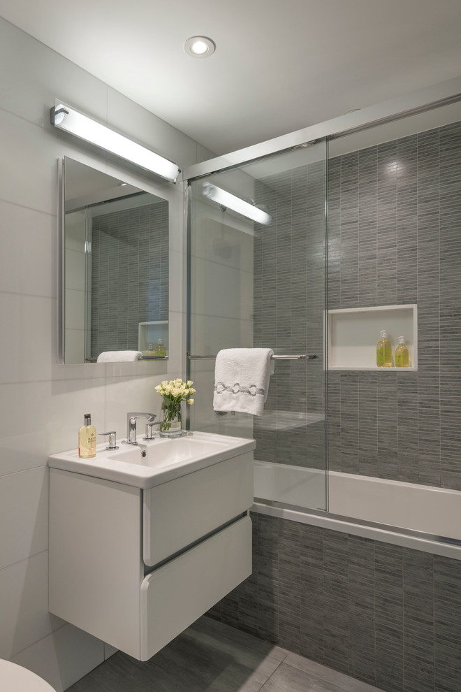 Modelo de cuarto de baño contemporáneo con bañera empotrada, combinación de ducha y bañera, baldosas y/o azulejos grises, armarios tipo mueble, puertas de armario blancas, baldosas y/o azulejos de cerámica, aseo y ducha y lavabo integrado