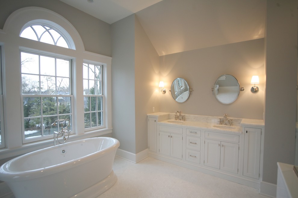 На фото: большая главная ванная комната в стиле фьюжн с раковиной с несколькими смесителями, фасадами с утопленной филенкой, белыми фасадами, мраморной столешницей и отдельно стоящей ванной с