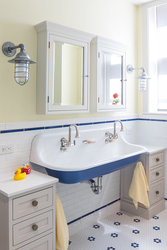 Klassisk inredning av ett badrum för barn, med skåp i shakerstil, beige skåp, blå kakel, vit kakel, gula väggar, mosaikgolv, ett avlångt handfat och vitt golv