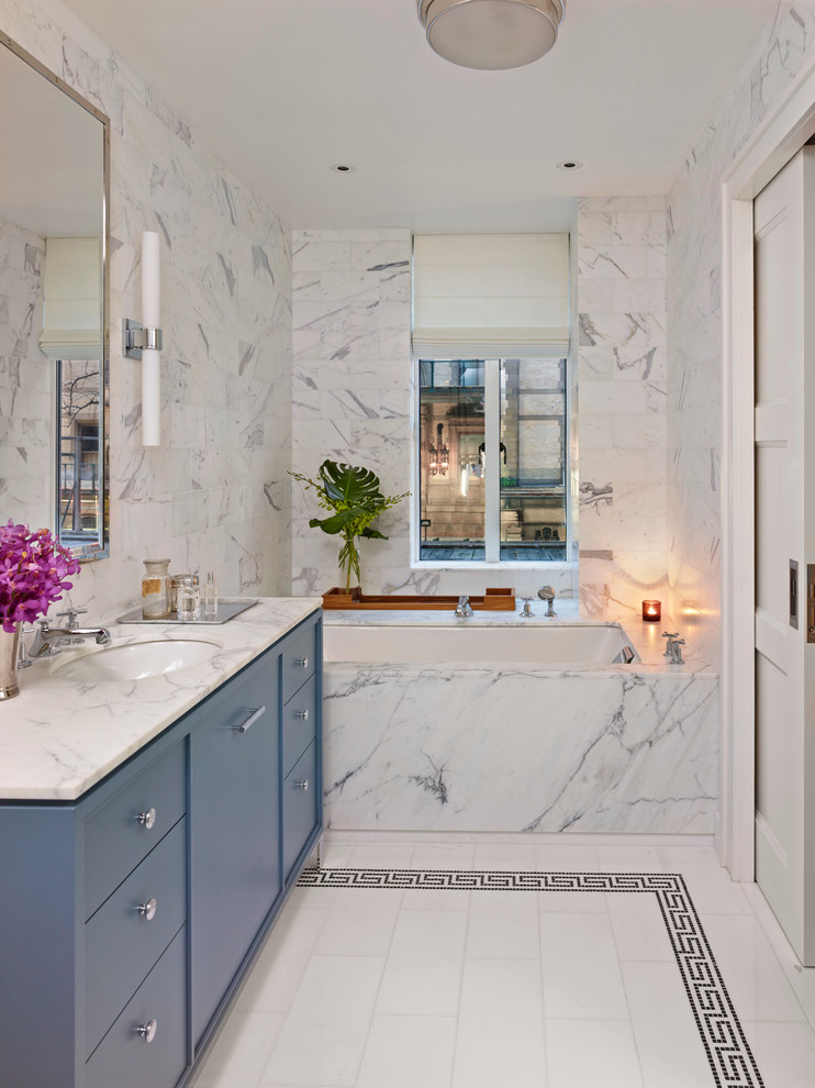 Идея дизайна: главная ванная комната среднего размера в современном стиле с врезной раковиной, плоскими фасадами, синими фасадами, полновстраиваемой ванной, белой плиткой, белыми стенами, плиткой из листового камня, мраморной столешницей, белым полом и белой столешницей