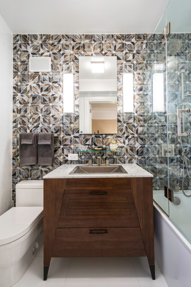 This is an example of a medium sized contemporary shower room bathroom in New York with a built-in sink, dark wood cabinets, an alcove bath, a shower/bath combination, multi-coloured tiles, white walls, a two-piece toilet, mosaic tiles, ceramic flooring, marble worktops and flat-panel cabinets.