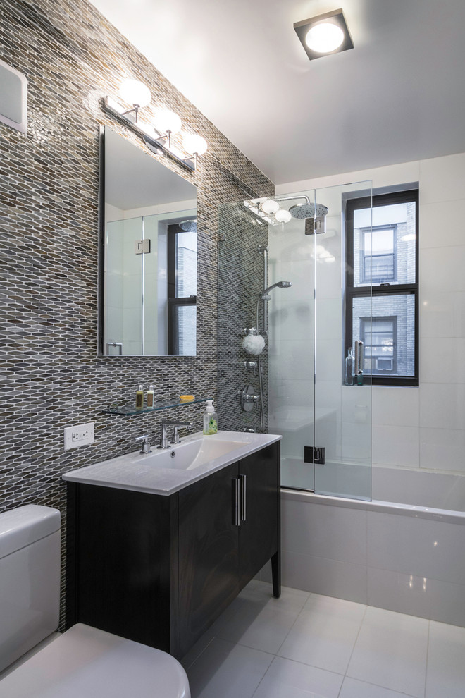 Exemple d'une salle d'eau tendance de taille moyenne avec des portes de placard noires, une baignoire en alcôve, un combiné douche/baignoire, WC séparés, un carrelage gris, mosaïque, un mur gris, un sol en carrelage de porcelaine, un lavabo intégré, un placard à porte plane et une fenêtre.