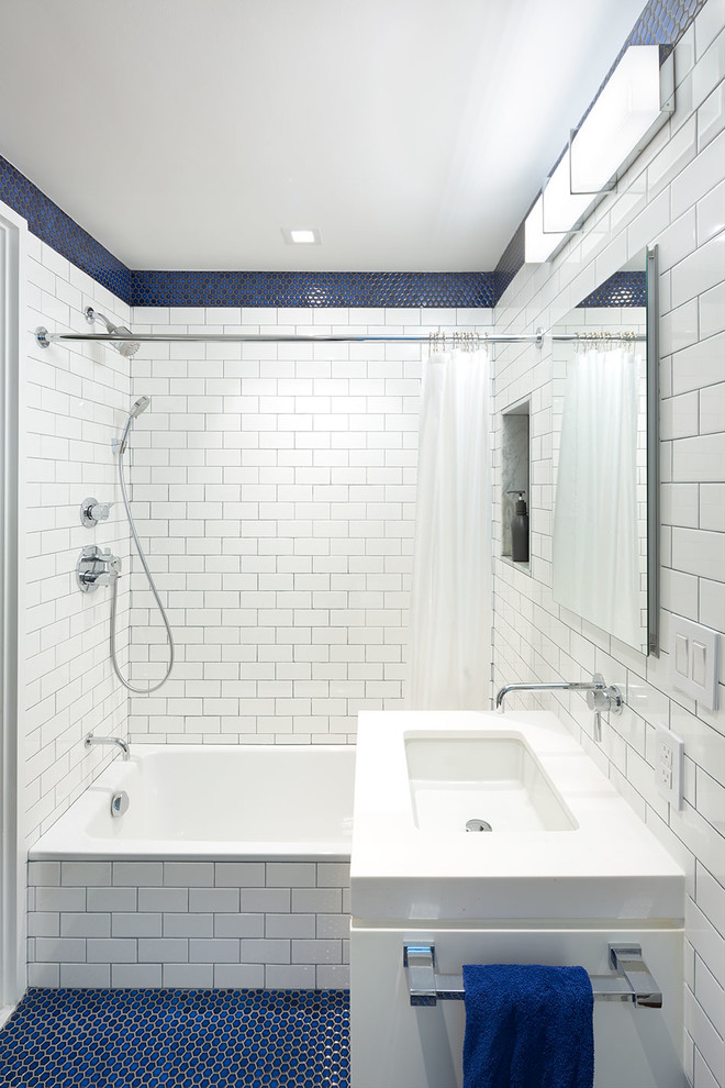This is an example of a medium sized contemporary family bathroom in New York with flat-panel cabinets, medium wood cabinets, a corner shower, a one-piece toilet, blue tiles, metro tiles, blue walls, ceramic flooring, a submerged sink, solid surface worktops, blue floors and white worktops.