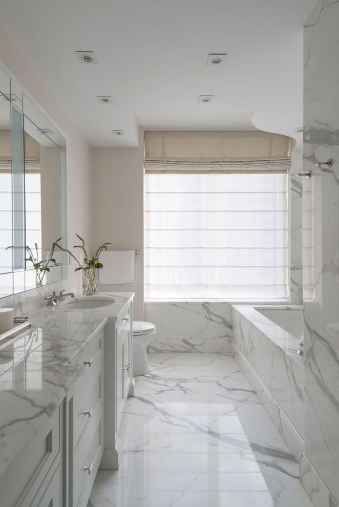 На фото: главная ванная комната в классическом стиле с врезной раковиной, фасадами с утопленной филенкой, белыми фасадами, полновстраиваемой ванной, бежевыми стенами и мраморной плиткой с