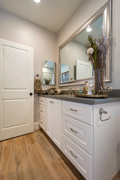 Inspiration for a medium sized traditional family bathroom in Phoenix with raised-panel cabinets, white cabinets, a built-in bath, an alcove shower, grey tiles, porcelain tiles, grey walls, porcelain flooring, a built-in sink, quartz worktops, brown floors and a shower curtain.
